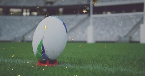 Rugby ball standing on tee with gold star confetti on stadium pitch closeup for kickoff