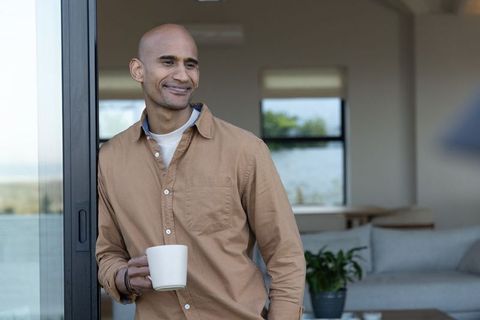 Man standing at sliding door holding coffee mug in contemporary neutral living room