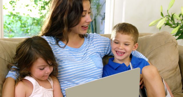 Mother and her two children sitting on a couch using a laptop together. This can be used for concepts such as family bonding, learning technology, and home life interactions. Ideal for advertisements, parenting blogs, and educational materials.