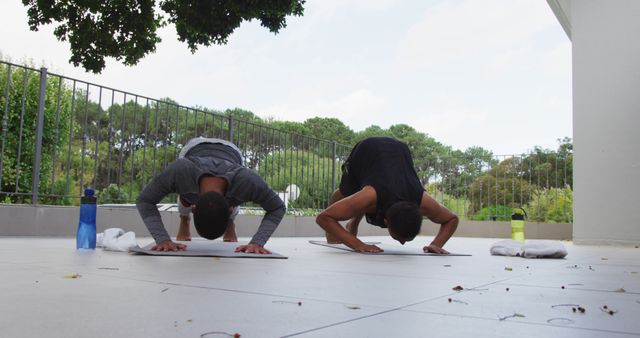 Biracial gay male couple standing on terrace practicing yoga. staying at home in isolation during quarantine lockdown.