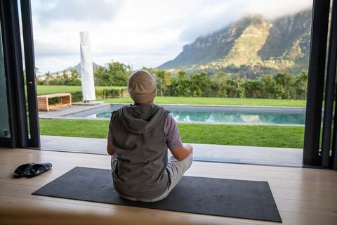 Meditating on yoga mat at open sliding doors overlooking pool and mountain vista
