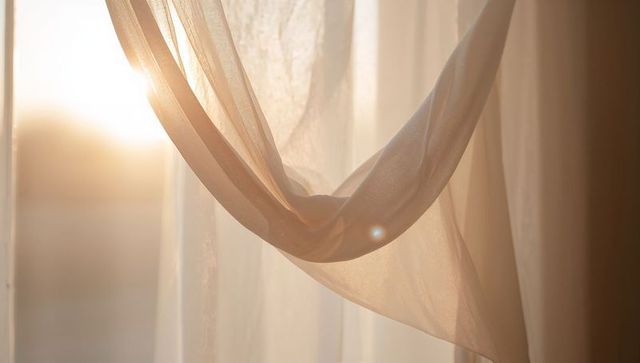 Sheer voile curtain knotted drape backlit by warm morning sunlight with lens flare