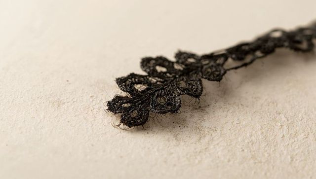 Lying frayed black floral lace trim on textured beige surface closeup with copy space