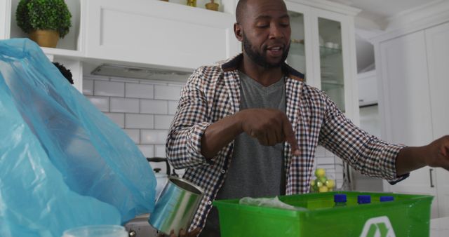 Man sorting recyclable items into a green recycling bin in a modern kitchen. Promotes eco-friendly and sustainable living, emphasizing environmental responsibility. Suitable for topics on waste management, recycling campaigns, environmental awareness, green living tips, and household sustainability practices.