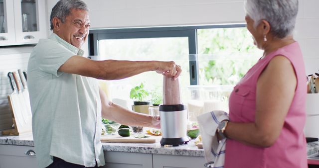 Senior couple happily making smoothies together in a modern kitchen. Ideal for use in materials promoting healthy lifestyles, active aging, senior health, or home and kitchen settings.