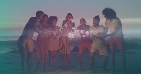 Friends holding sparklers on beach at twilight laughing barefoot along shoreline