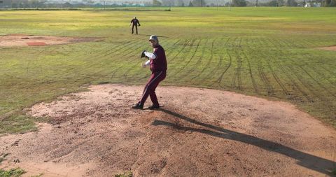 Pitcher and Fielder in Maroon Uniforms on Baseball Field