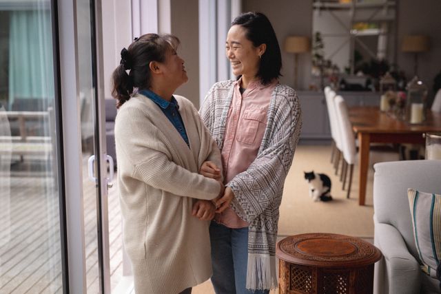 Two senior Asian women standing and talking at home, creating a warm and friendly atmosphere. Ideal for use in articles or advertisements about senior lifestyle, family bonding, and home living. Perfect for illustrating themes of friendship, aging, and everyday life.