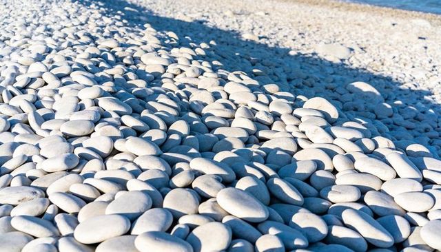 Sunlit smooth white pebbles forming rhythmic coastal pattern on azure shoreline