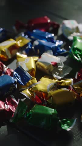 Vertical moving camera revealing foil-wrapped candies on dark tabletop with shimmering highlights