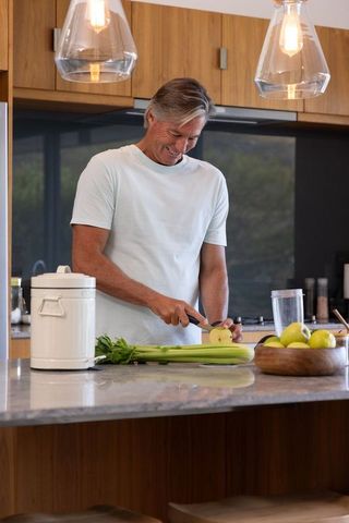 Mature man slicing green apple on kitchen island with warm wood cabinetry