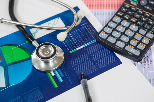 Stethoscope lying on desk with financial charts, calculator, and pen, representing intersection of healthcare and finance. Useful for illustrating medical business analysis, healthcare economics, financial planning in healthcare, and professional office environments.