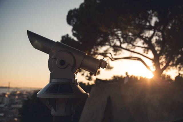 The photo depicts a telescope positioned outdoors with the sun setting behind it. It brings attention to the theme of exploration, observation, and appreciating scenic views. Suitable for use in travel blogs, astronomy-related articles, outdoor leisure content, and inspirational, nature-themed websites.