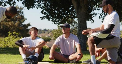 Young men sitting on grass after baseball practice discussing strategy and teamwork
