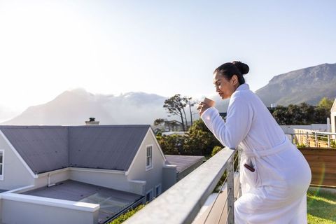 Asian woman enjoying morning coffee on balcony in robe with mountain sunrise view