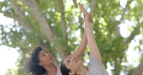 Diverse friends stretching together under sunlit park trees, partner yoga support and balance