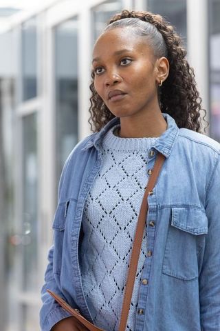 Thoughtful african woman wearing denim jacket knit sweater and crossbody bag on city street