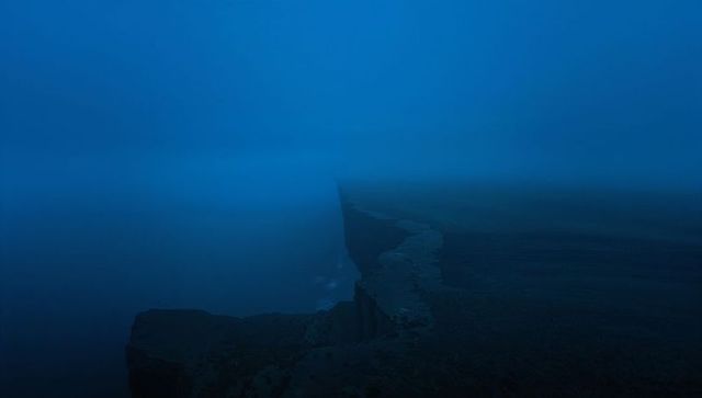 Moody foggy cliff headland at twilight with narrow jutting path vanishing into sea mist