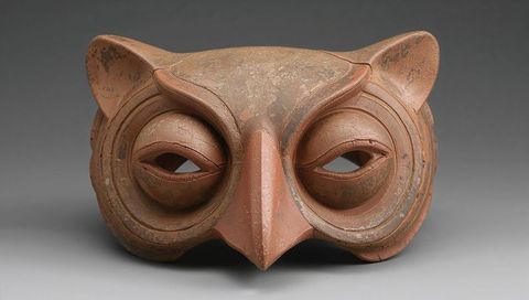 Terracotta owl mask featuring stylized beak, layered eye rings and weathered surface