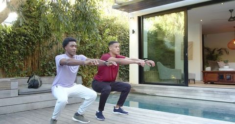 Two Male Friends Doing Squats by Pool in Modern Outdoor Setting