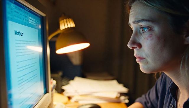 Late-night writer working at computer with weary expression and warm desk lamp glow