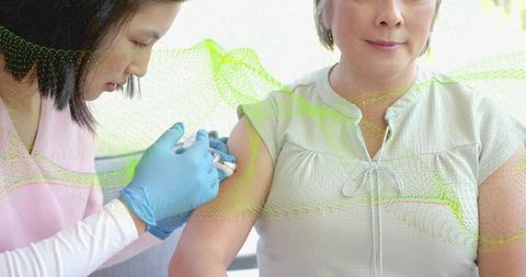 Nurse administering vaccine to middle-aged Asian woman in clinic with green data overlay