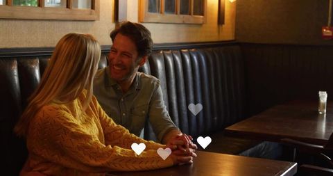 Couple holding hands in cozy pub booth during candlelit romantic date night