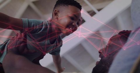 Father lifting son, sharing joyful gaze with pink digital network overlay, playful home bonding