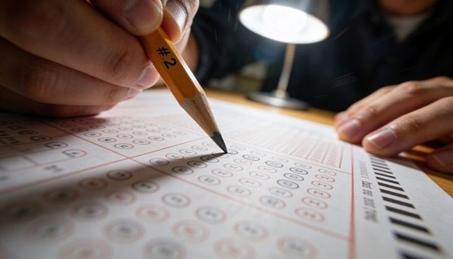Filling scantron bubbles with #2 pencil under desk lamp showing exam focus