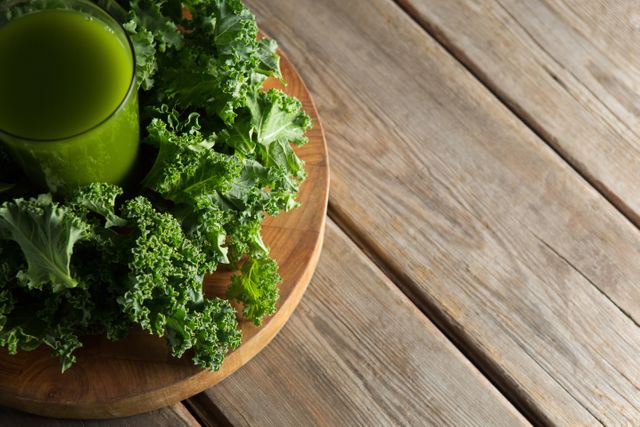 High angle view of fresh kale juice in a glass surrounded by kale leaves on a wooden table. Ideal for use in health and wellness blogs, nutrition articles, vegan and vegetarian recipe websites, and promotional materials for organic food products.