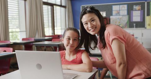 Smiling Teacher with Schoolgirl Using Laptop in Classroom
