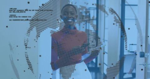 Smiling professional holding tablet behind dotted world map on glass partition in office