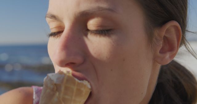 Happy caucasian woman eating ice cream at beach on sunny day. Vacation, summer, nature and food, unaltered.