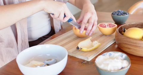Woman slicing grapefruit on wooden cutting board for fresh breakfast bowl