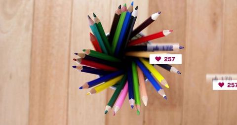 Top-down fanned colored pencils in cup on light wooden table with social like badges