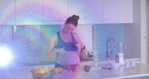Pregnant woman preparing fresh fruit smoothie at modern kitchen island with blender