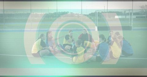 Female athletes sitting in team huddle on synthetic turf leaning and listening