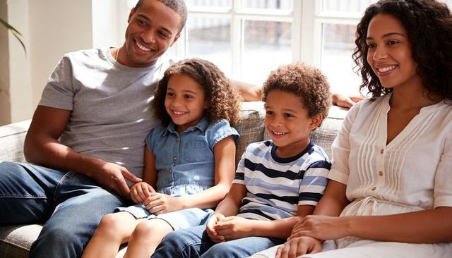 Family of four relaxing on sofa in bright living room smiling together in casual clothing