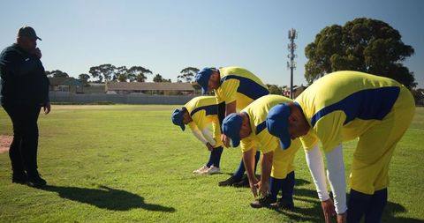 Cricket team stretching in yellow and blue uniforms with coach supervising on sunny field