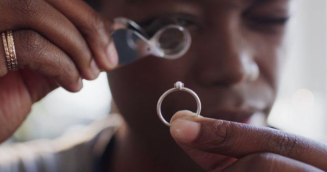 African american female jeweller looking at jewellery through magnifying glass in jewellery shop. Jewellery, enterpreneurship and small business, unaltered.