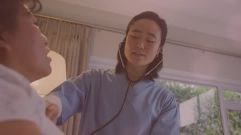 Caring Asian Doctor Examining Patient at Home with Light Spot Overlays