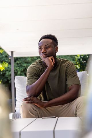 African american man sitting on patio sofa contemplating with smartphone on table