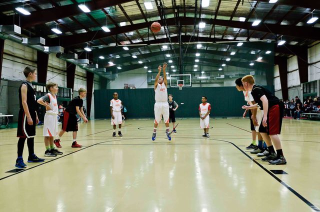 Group of boys playing basketball in an indoor gymnasium. One player shooting a free throw while others watch. Ideal for content about youth sports, teamwork, school competitions, and physical education programs.