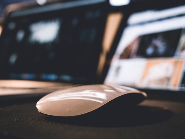 Modern wireless mouse on desk in front of blurred computer screens. Ideal for illustrating topics related to office work, technology, digital devices, productivity, and modern workspace setups.