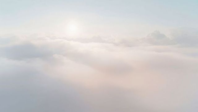 Sunlit cloudscape glowing over misty horizon, sunbeams dancing through airy sky