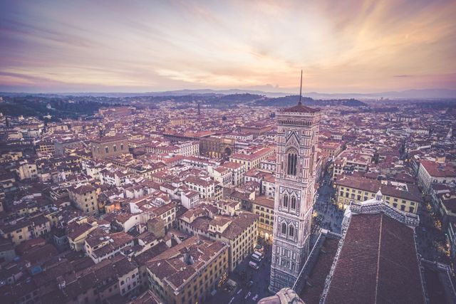 Shows a panoramic aerial view of Florence, Italy, with sunset casting warm hues over historic buildings and the iconic Duomo. Ideal for content related to travel, architecture, European destinations, historical sites, and cultural tourism.