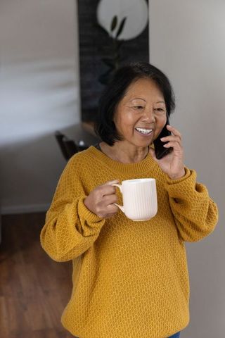 Senior woman enjoying phone call with coffee in comfortable home environment