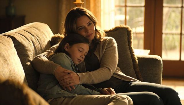 Mother embracing sleeping daughter on sofa in warm sunlit living room cozy family moment