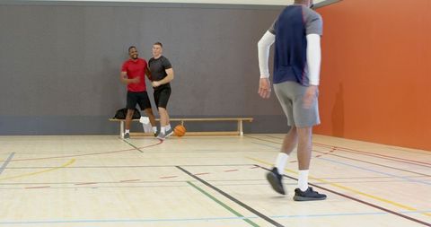 Walking player crossing indoor basketball court while teammates laughing on bench