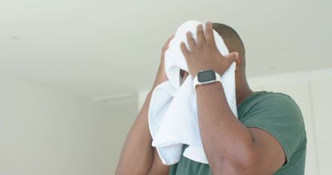 African american man drying face with towel and wearing smartwatch in minimalist interior